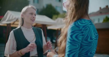 Genç sarışın kadın, güneşli bir günde kız arkadaşıyla konuşuyor.