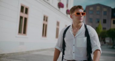 Hafta sonu güneşli bir günde şehirde yürürken şık güneş gözlüğü takan yakışıklı bir adam.