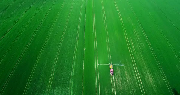 Agriculture Aerial Of Tractor Spraying Farm Land With Pesticides, agricultural chemicals. Drone shoot of farming Equipment. Food Modification GMO Farming Concept.