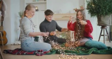 Parlayan ışıkları olan gülümseyen kadın ve erkek arkadaşlar Noel tatilinde evde oturuyorlar.