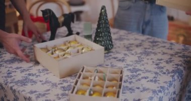 Kadın ve erkek arkadaşlarının orta kesimi tatil sırasında evdeki masaya Noel süsleri koyuyor.