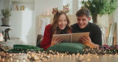 Mutlu genç çift Noel tatili boyunca oturma odasında uzanmış fotoğraf albümüne bakıyor.
