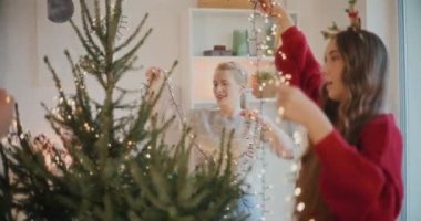 Genç erkek ve bayan arkadaşlar evdeki Noel ağacında parlayan ışıkları ayarlıyorlar.
