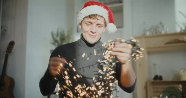 Junger Mann Trägt Nikolausmütze Beim Sortieren Glühender Lichter Für Weihnachtsdekoration — Stockvideo