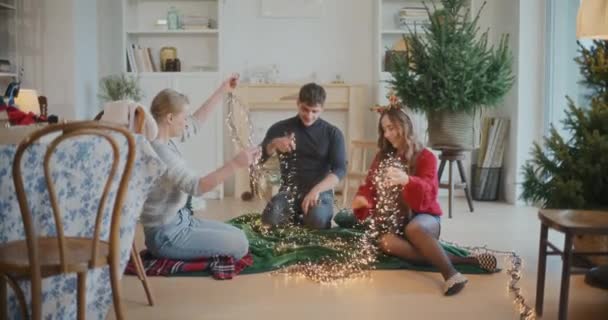 年轻的男女朋友们在家里整理纠结在一起的照明灯作为圣诞装饰 — 图库视频影像
