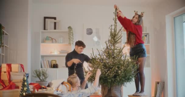 假日期间 男人和女人在客厅里点着灯装饰圣诞树 — 图库视频影像