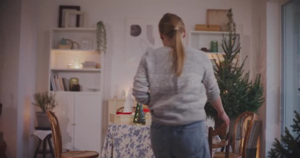 在家里客厅里把圣诞长袜放在一张张桌子上的年轻女人 — 图库视频影像