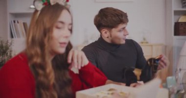 Genç erkek ve kadın arkadaşlar ellerinde Noel süsleri tutarken birbirleriyle konuşuyorlar.