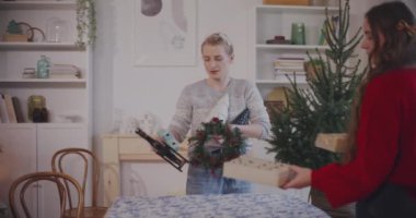 Genç bayan ve erkek arkadaşları tatil sırasında evdeki masaya Noel süsü koyuyorlar.