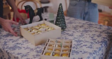Kadın ve erkek arkadaşlarının orta kesimi tatil sırasında evdeki masaya Noel süsleri koyuyor.