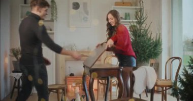 Genç adam ve kadın Noel boyunca oturma odasında masa düzenliyorlar.