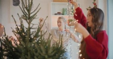 Genç erkek ve bayan arkadaşlar evdeki Noel ağacında parlayan ışıkları ayarlıyorlar.