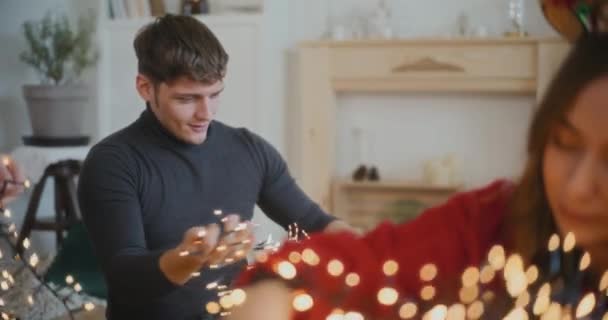 Young Man Sorting Tangled Illuminated Lights Female Friends Home Christmas — Stock Video