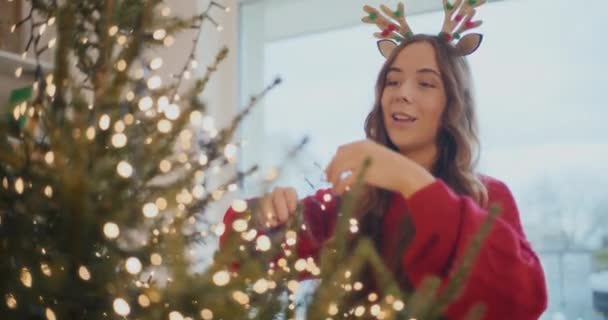 Glimlachende Jonge Vrouw Aanpassen Van Led Verlichting Kerstboom Thuis Tijdens — Stockvideo