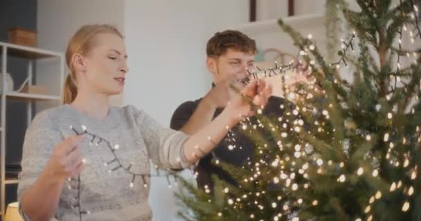 男人和女人的朋友在家里用彩灯装饰圣诞树 — 图库视频影像