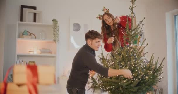 假期期间 男友和女友在家里用彩灯装饰圣诞树 — 图库视频影像