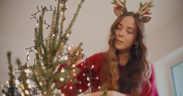 Wanita Muda Yang Mendekorasi Pohon Natal Dengan Lampu Bersinar Rumah — Stok Video