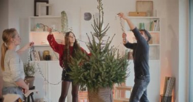 Genç adam ve kadınlar tatilde Noel ağacının ışıklarını düzeltiyorlar.