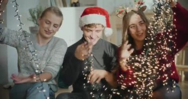 Evde Noel süsü olarak birbirine dolanmış parlak ışıkları sıralayan erkek ve kadınlar.