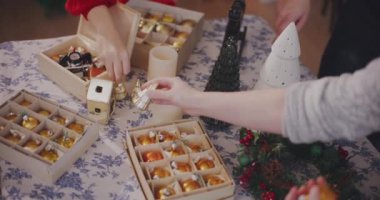 Kırpılmış genç erkek ve kadın arkadaşlarının elleri evdeki masaya Noel süsü koyuyor.
