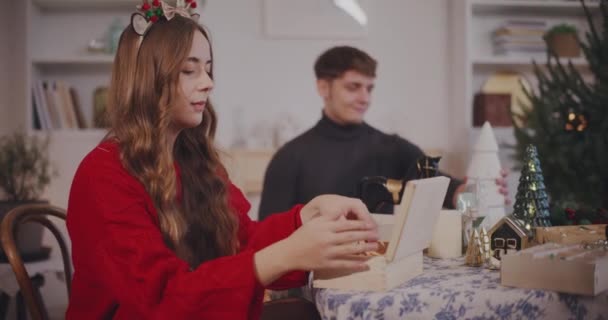 年轻女人坐在桌旁给男朋友献上圣诞装饰品 — 图库视频影像