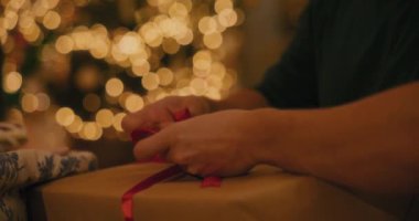 Evde Noel hediyesi kutusuna kurdele bağlayan bir adam.