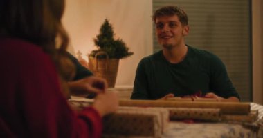 Hediye kutularıyla gülümseyen adam Noel arifesinde evde otururken kız arkadaşlarıyla konuşuyor.