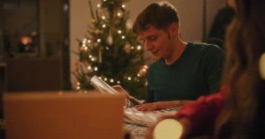 Gülümseyen genç adam Noel hediyesini paketliyor. Tatil boyunca evde bayan arkadaşının yanında oturuyor.