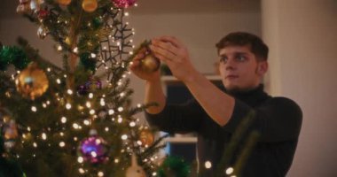 Evdeki aydınlanmış Noel ağacını süslerken takı bağlayan genç adam.