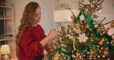 Noel boyunca oturma odasında Xmas ağacını süslerken takı bağlayan genç bir kadın.