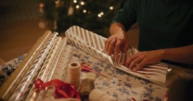 Noel arifesinde erkeklerin hediye paketini masanın üstünde paketlemelerinin orta kısmı.