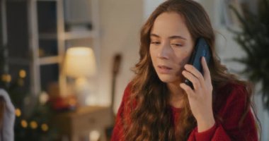 Noel 'de evde otururken cep telefonu kullanan üzgün genç bir kadın.