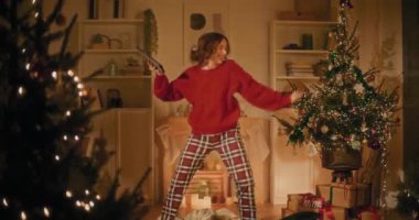 Noel arifesinin tadını çıkarırken evde dijital tabletle dans eden mutlu genç kadın.
