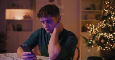 Genç adam gece boyunca oturma odasında otururken akıllı telefon kullanıyor.