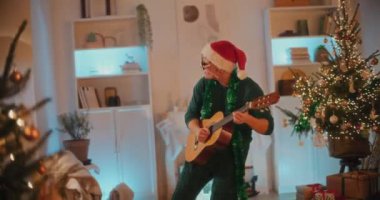 Genç adam Noel boyunca oturma odasında dikilirken gitar çalmaktan hoşlanır.