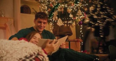 Mutlu genç çift Noel arifesinde evde fotoğraf albümü izliyor.