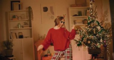 Güneş gözlüğü takan genç bir kadın Noel boyunca evde dans ederken eğleniyor.