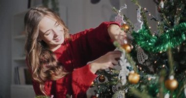 Mutlu, genç, güzel bir kadın Noel ağacını çeşitli süslerle süslüyor.