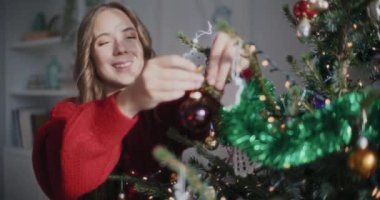 Neşeli, genç ve güzel bir kadın güneşli bir evde Noel ağacında takılıyor.