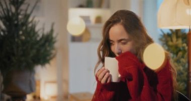 Genç bir kadın Noel tatili boyunca oturma odasında otururken kahve kokusu alıyor.