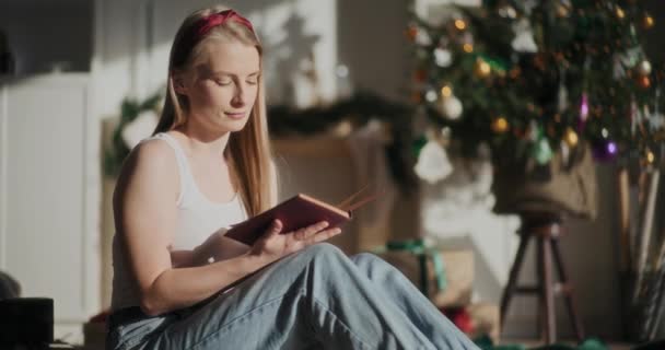 Красивая Молодая Женщина Читает Книгу Сидя Дома Елкой Заднем Плане — стоковое видео