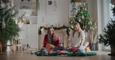 Güzel genç kız kardeşler evde otururken paketlenmiş Noel hediyeleriyle kurdele bağlıyorlar.