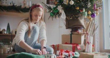 Güzel genç bir kadın evde otururken Noel hediyelerini paketliyor.