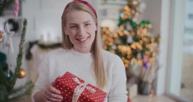 Noel hediyesini elinde tutan neşeli, genç bir kadının portresi.
