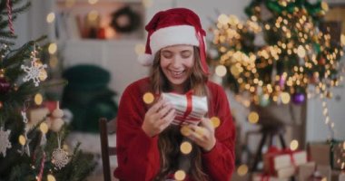 Noel Baba şapkalı neşeli genç kadın Noel boyunca dekore edilmiş eve hediye kutusu atıyor.
