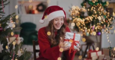 Noel Baba şapkalı heyecanlı genç kadın Noel boyunca süslü evde hediye kutusuyla oynuyor.
