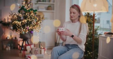 Güzel genç bir kadın Noel zamanı evdeki sandalyesinde kahve içerken gülümsüyor.