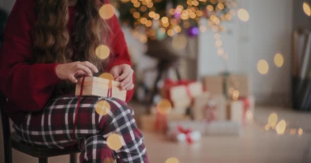 自宅でクリスマス中に椅子に座っている間 木製のギフト用の箱にリボンを結ぶ若い女性のミックス — ストック動画