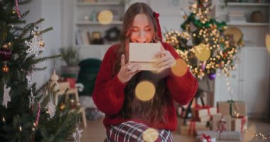 Şaşırtıcı neşeli kadın Noel 'de evinde sandalyesinde otururken tahta hediye kutusundan kolyeyi çıkarıyor.