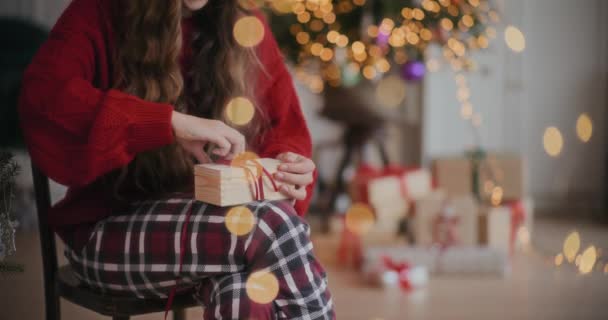 陽気でかわいい若い女性はクリスマスの間に装飾された家に座っている間照らされた木製のギフト用の箱を開けます — ストック動画